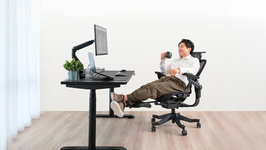 Person reclining in an ergonomic chair while enjoying a cup of coffee at a modern workspace, featuring a sleek desk setup with a computer and potted plant.