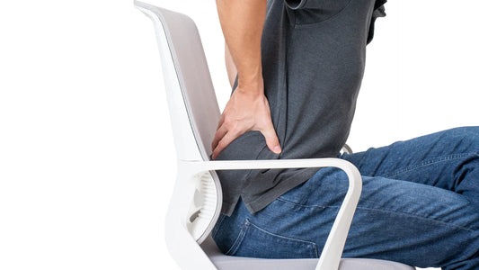 Person sitting in a chair and holding their lower back, illustrating discomfort from poor lumbar support.